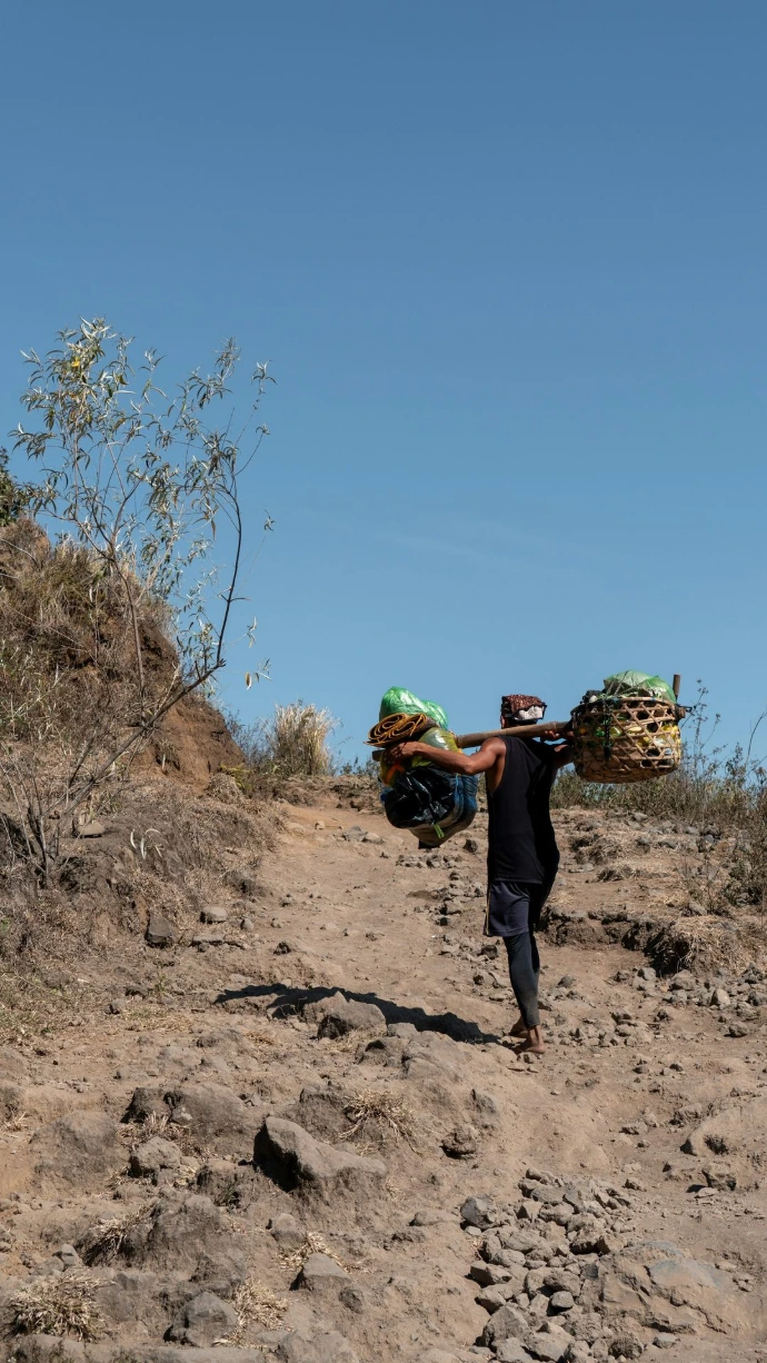 A man walking down a dirt road carrying bags